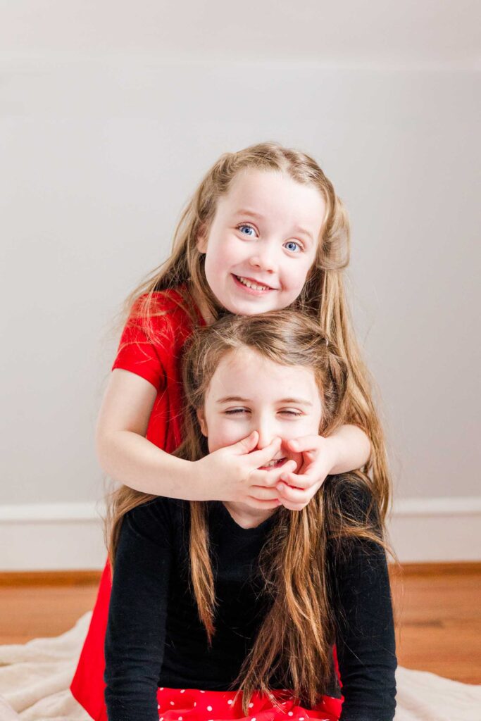 Young girl playfully squeezes other girl's nose during photo session by a Main Line sensory and autism friendly photographer.