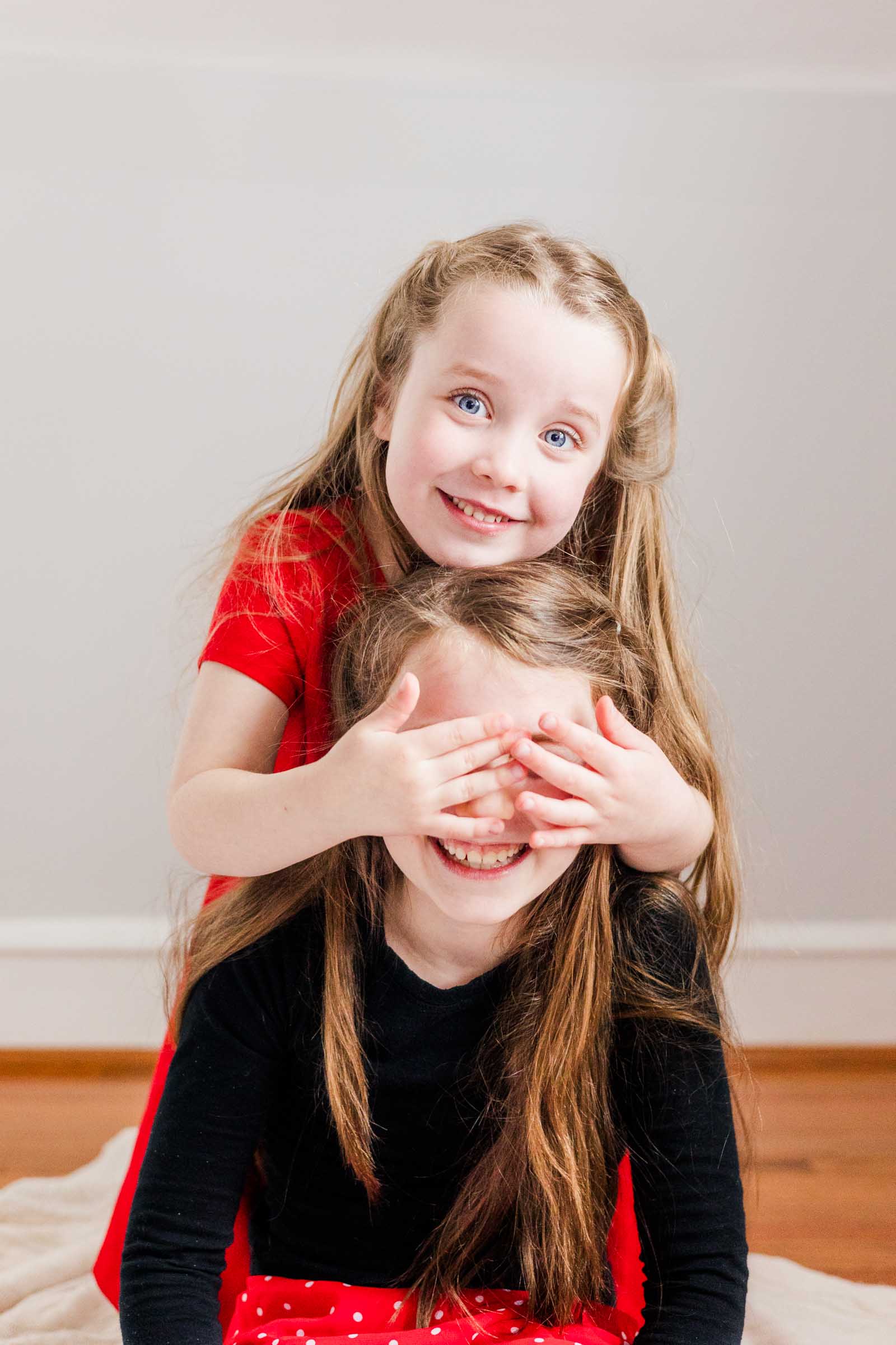 Two young girls playfully interact during Main Line photo session. One girl covers the other's eyes.