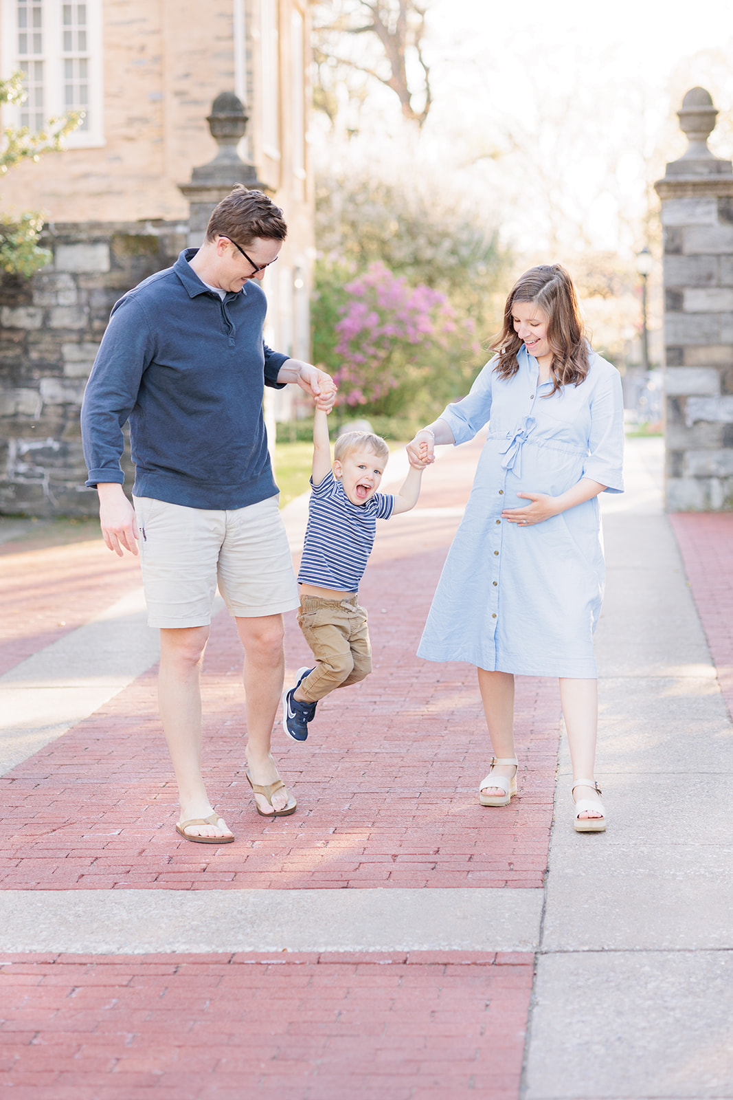 Parents lift toddler as they walk down brick path