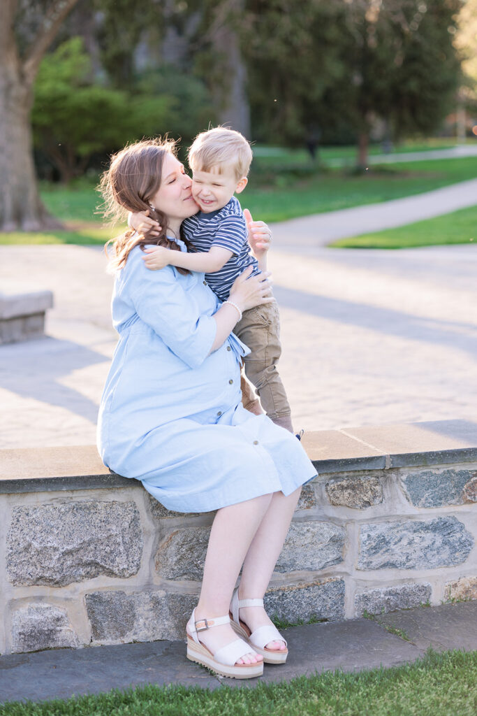 Seated mother hugs her toddler son on stonewall at Haverford arboretum.