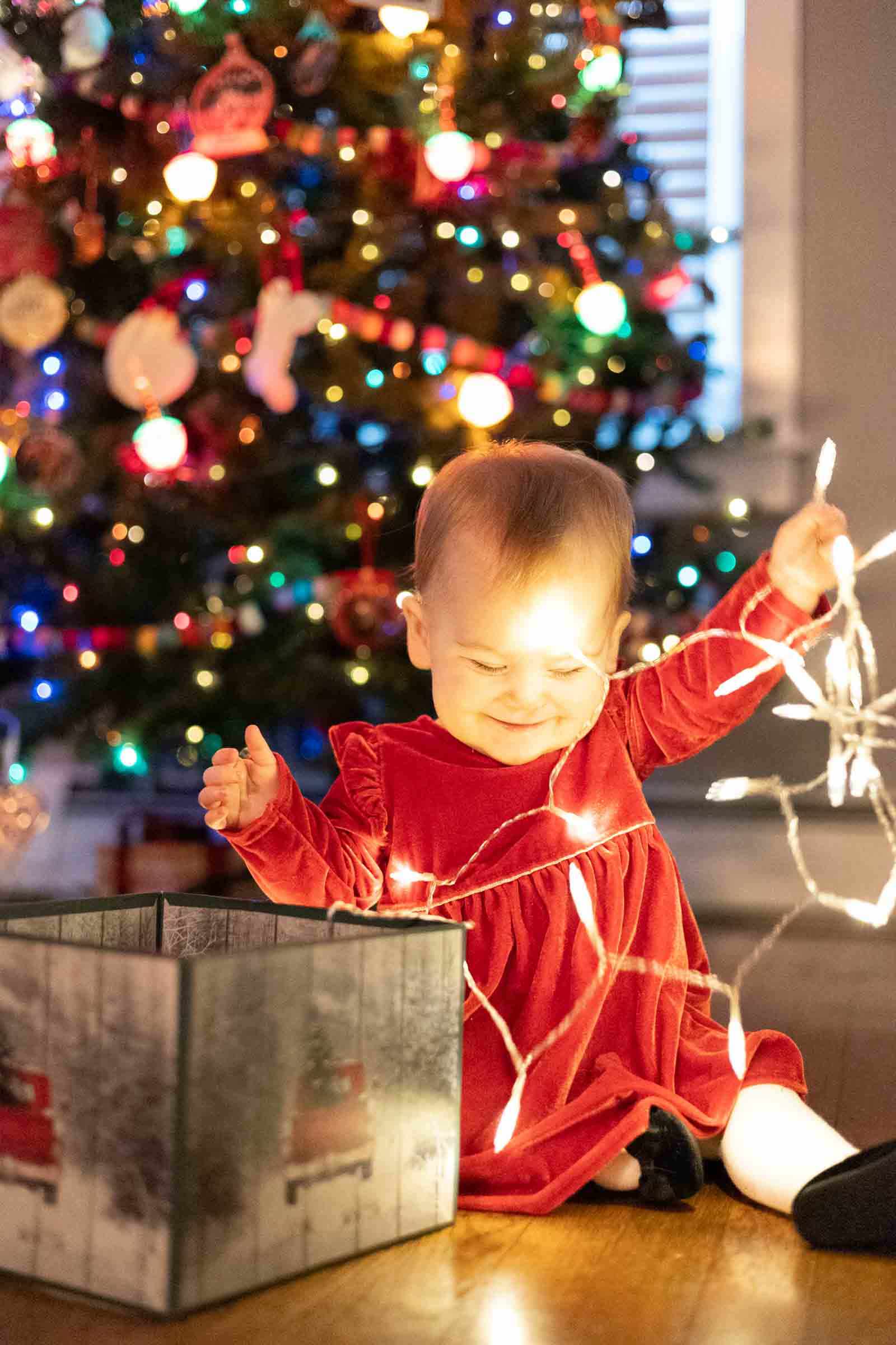 Baby pulls string lights from box during Christmas baby portrait session