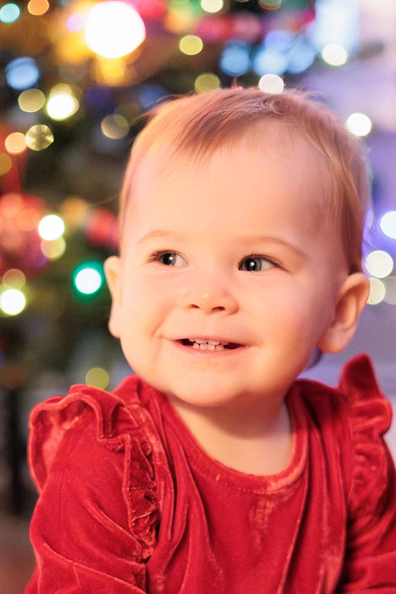 Baby smiles in front of Christmas tree during baby portrait session