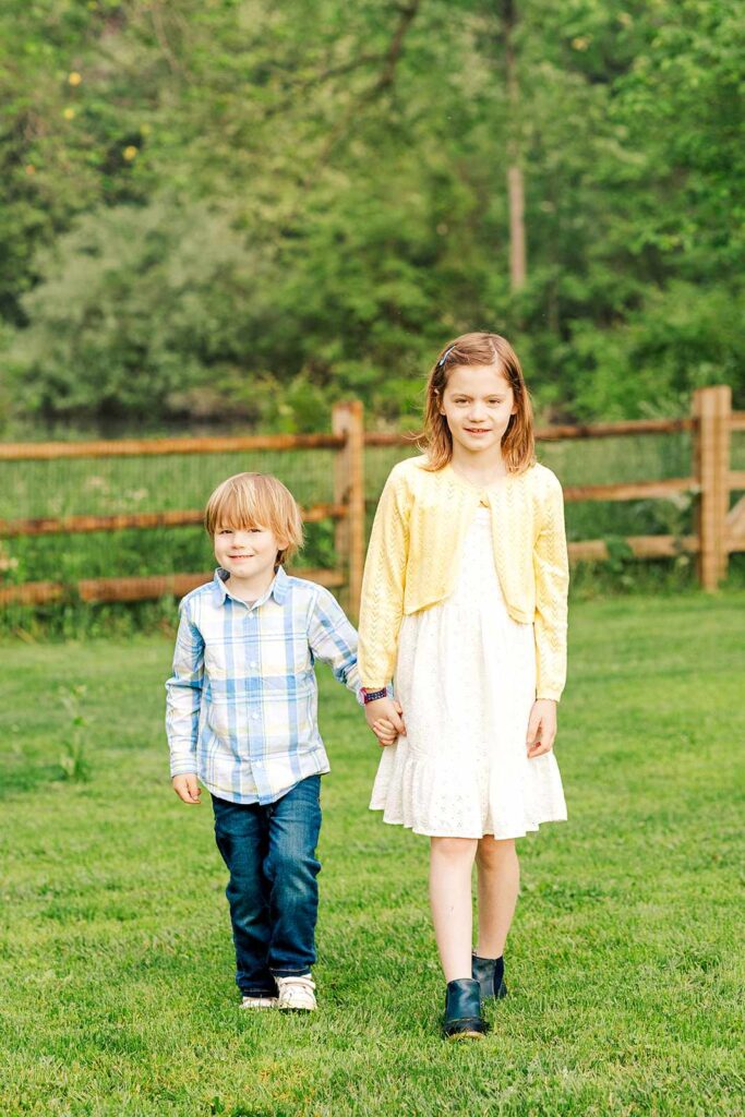 Young girl and boy walk while holding hands in field by pond, Haverford, PA