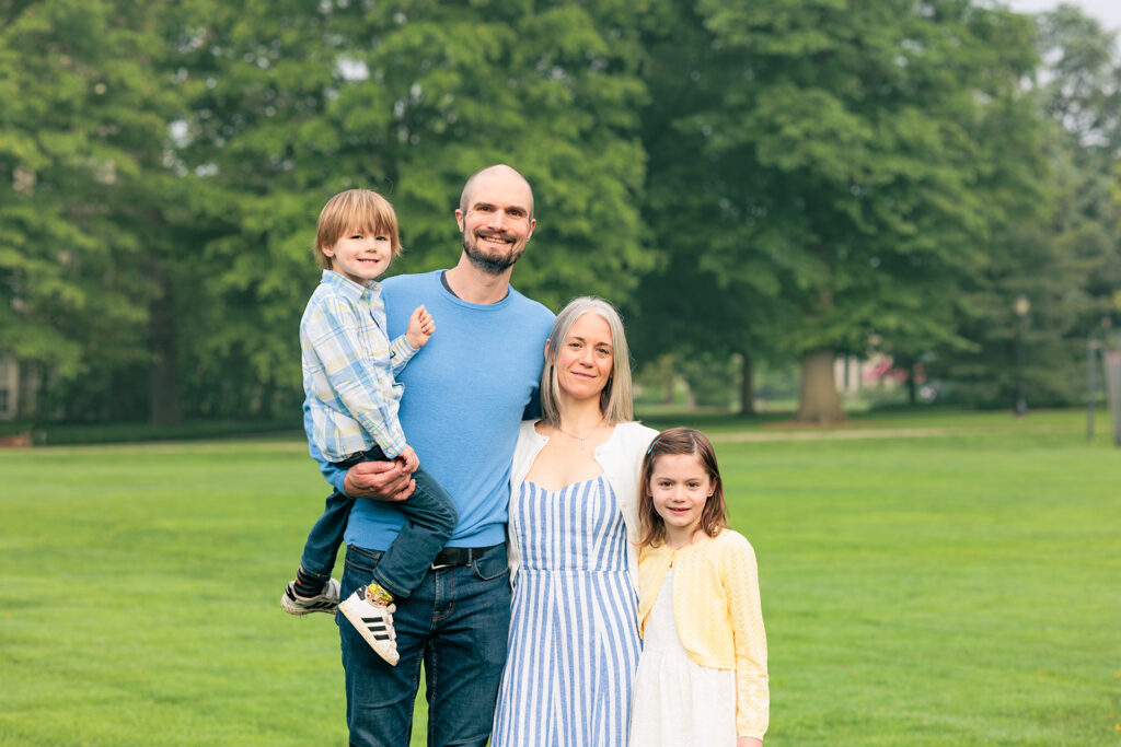 Family of four faces camera in field in during family photo session