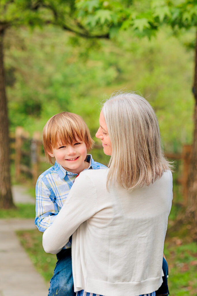 Young boy looks over mother's shoulder as she smiles at him. 