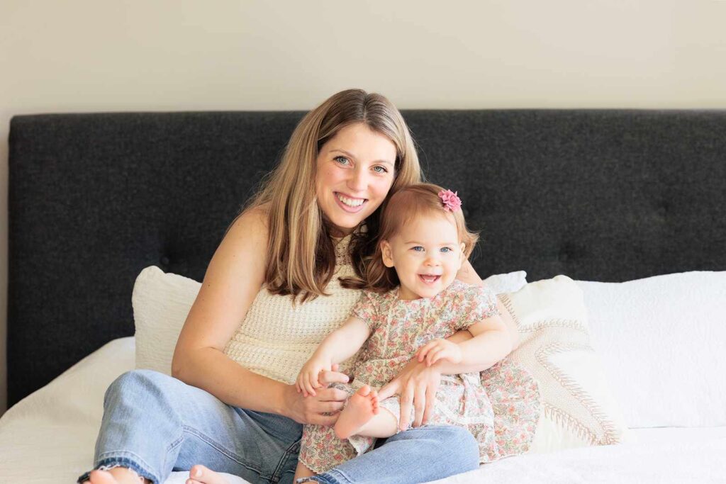 Mom and toddler smile at camera during newborn photo session