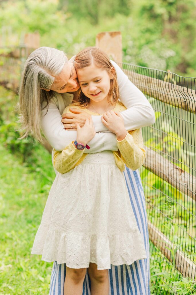 Mother hugs young girl while whispering in her ear during Haverford family photo session. 