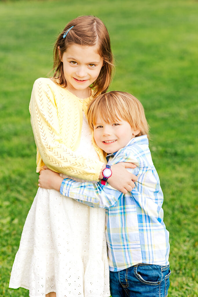 Young girl and boy hug one another while looking at the camera.