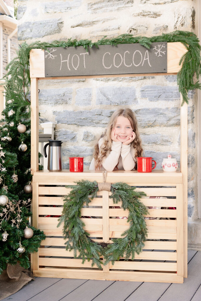 Girl smiles behind hot chocolate stand for main line holiday mini session in Narberth, PA