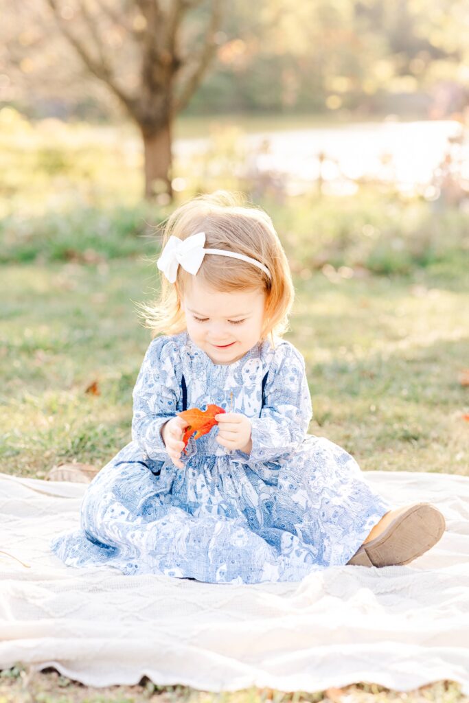 Toddler girl plays with leave during family photo session in the fall.